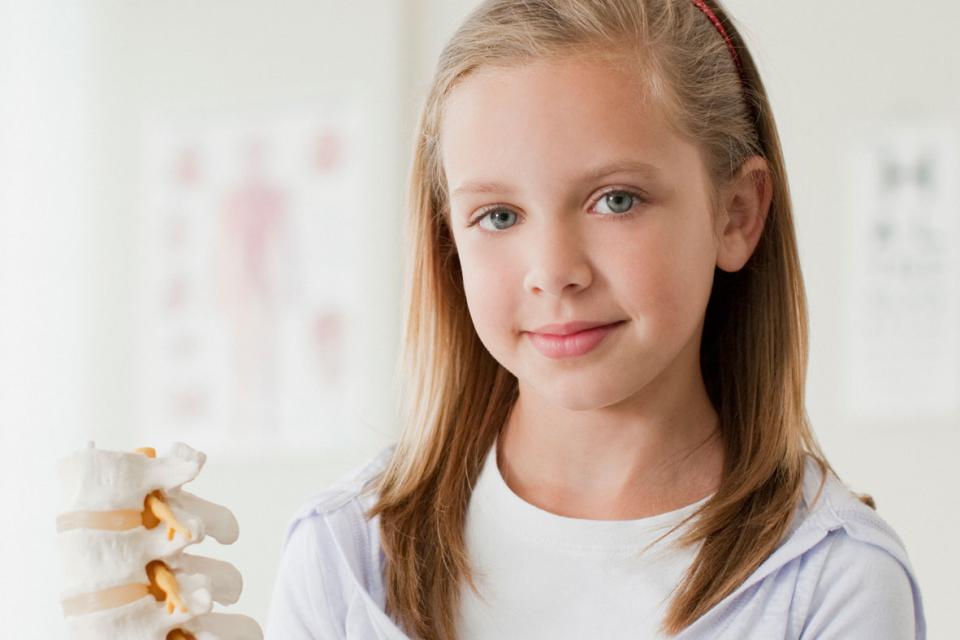Petite fille regardant la caméra en tenant le squelette d'une colonne vertébrale