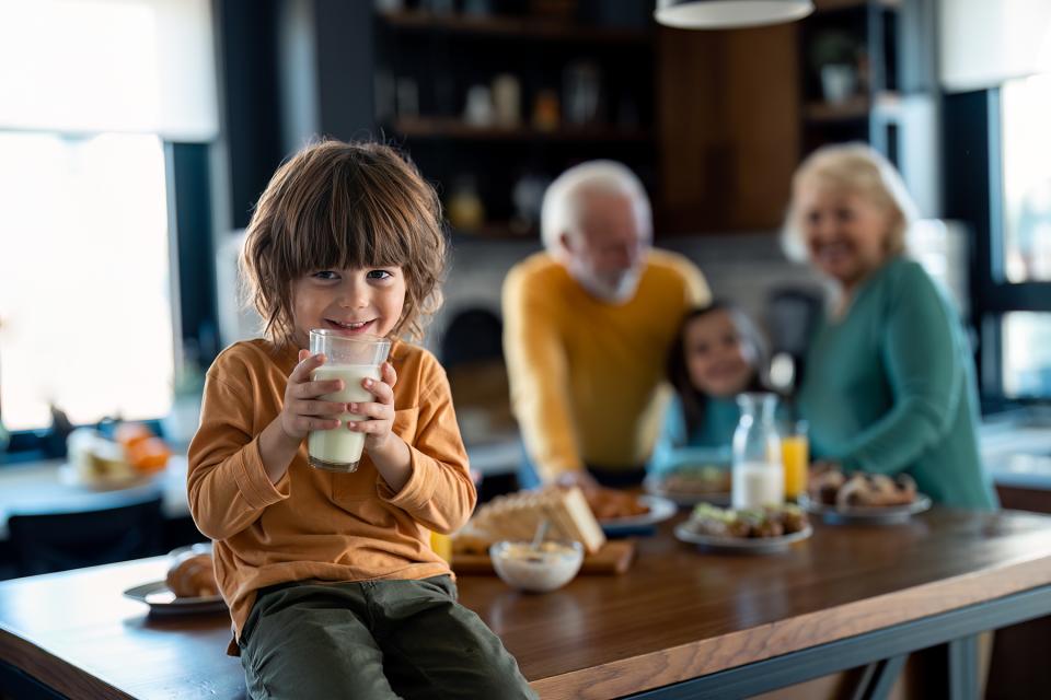 little boy sitting on the counter holding a glass of milk