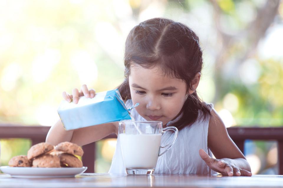 Petite fille versant soigneusement du lait dans son verre