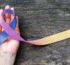 Hand holding a blue and purple cancer ribbon
