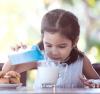 Little girl carefully pouring milk into her glass