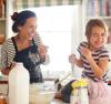 Mother and daughter baking and laughing in the kitchen with a litre of milk on the counter